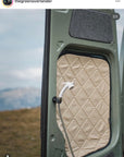Tactic Engineering magnetic shower mount in use on campervan sliding door, white shower head magnetically attached to van exterior with quilted door insulation visible, scenic mountain landscape in background, vanlife outdoor shower by @thegreenoverlander