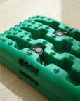 Close up of two Tactic Engineering magnetic quick release mounts installed on green TRED recovery board, showing the stainless steel pins inserted through board mounting holes with safety cables attached for secure magnetic vehicle mounting