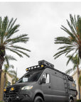 Rogue Vans matte black Mercedes Sprinter 4x4 Odyssey conversion with MaxTrax recovery boards on Tactic Engineering magnetic quick-release mounts, parked among palm trees