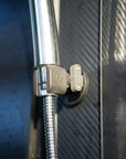 Close up of Tactic Engineering magnetic shower mount holding stainless steel shower hose on carbon fiber van surface, SLS 3D printed nylon clip with Tactic logo gripping the flexible hose securely with neodymium magnet base attached to vehicle body