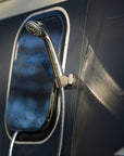 Stainless steel shower head magnetically mounted next to campervan window using Tactic Engineering magnetic shower mount, close up showing secure attachment on carbon fiber van exterior with water droplets visible, outdoor vanlife shower setup in use