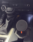 Tactic Engineering MagSafe phone mount installed in Toyota Land Cruiser 250 center console, Qi2 wireless charging pad with Qi2 logo visible, orange USB C cable connected, SLS 3D printed nylon mount base fitted in cupholder area