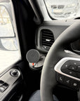 Tactic Engineering MagSafe phone mount installed on Iveco Daily dashboard, wider angle view showing mount position relative to steering wheel and air vents, Qi wireless charging pad with orange USB C cable visible on SLS 3D printed nylon base