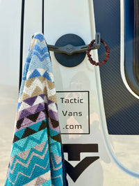 Tactic Engineering magnetic towel hook mounted on van exterior holding a colorful patterned beach towel, featuring neodymium magnet base with 55 kg pull force and rubber coated design for van life