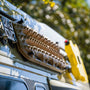 MaxTrax MK2 recovery boards mounted on blue van roof rack using Tactic Engineering magnetic quick release supports with stainless steel pins, close up showing the sand colored boards securely attached for off road adventure