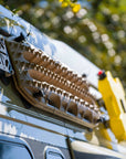 MaxTrax MK2 recovery boards mounted on blue van roof rack using Tactic Engineering magnetic quick release supports with stainless steel pins, close up showing the sand colored boards securely attached for off road adventure