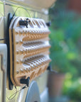 Close up of Tactic Engineering magnetic quick release supports holding MaxTrax MK2 recovery boards on van roof, showing stainless steel quick release pins and neodymium magnet bases with blurred greenery background