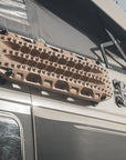 Overland van roof rack with sand colored recovery boards and yellow RotoPax fuel container magnetically mounted using Tactic Engineering magnetic plate, close up of roof gear setup showing pop top tent and off road expedition equipment