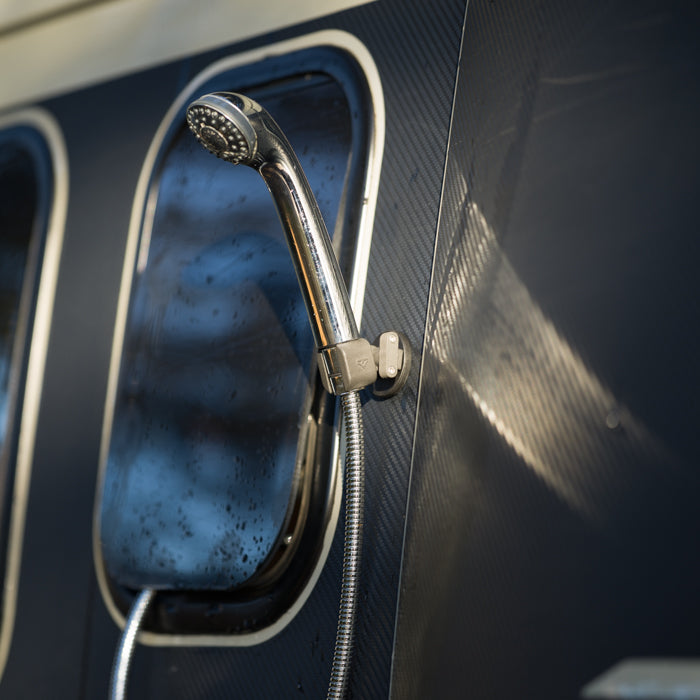 Close up of Tactic Engineering magnetic shower head holder mounted on van exterior with running water, showing secure magnetic attachment to vehicle body panel