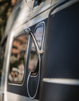 Tactic Engineering magnetic shower head holder mounted on van exterior near window with rain droplets, showing the compact magnetic mount securely holding the shower head hose against the vehicle body