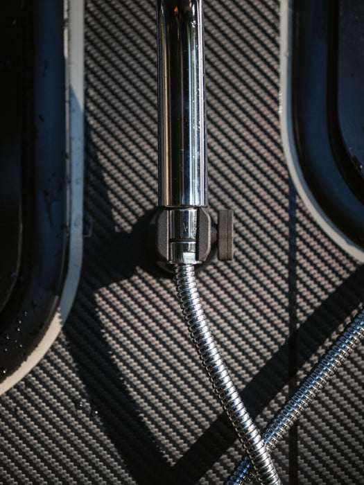 Tactic Engineering magnetic outdoor shower kit detail showing chrome shower head and flexible hose resting on carbon fiber textured van panel with magnetic mount visible