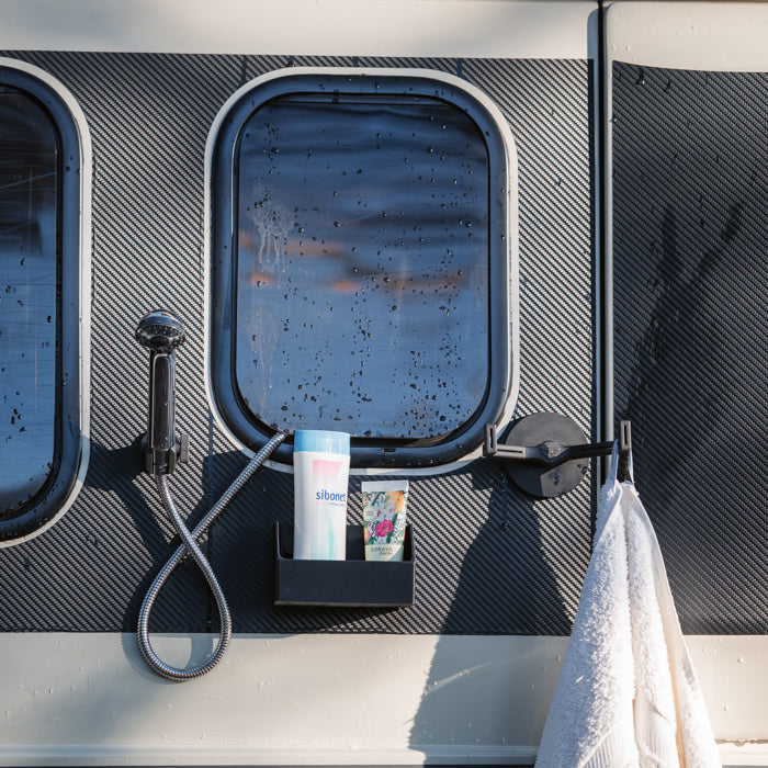 Tactic Engineering magnetic outdoor shower accessories mounted on van exterior in rainy weather, featuring magnetic shower head holder, shampoo bottle holder with toiletries and magnetic towel hook with white towel