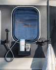 Tactic Engineering magnetic outdoor shower accessories mounted on van exterior in rainy weather, featuring magnetic shower head holder, shampoo bottle holder with toiletries and magnetic towel hook with white towel