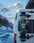 Close up of snowboard magnetically mounted on rear door of Mercedes Sprinter van using Tactic Engineering magnetic carrier in snowy mountain setting
