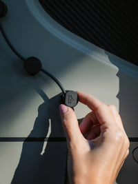 Hand placing Tactic Engineering Mini Clip magnetic cable holder on van interior panel, showing the compact clip holding a black cable in place with Tactic Engineering logo visible, demonstrating easy magnetic installation for campervan cable management