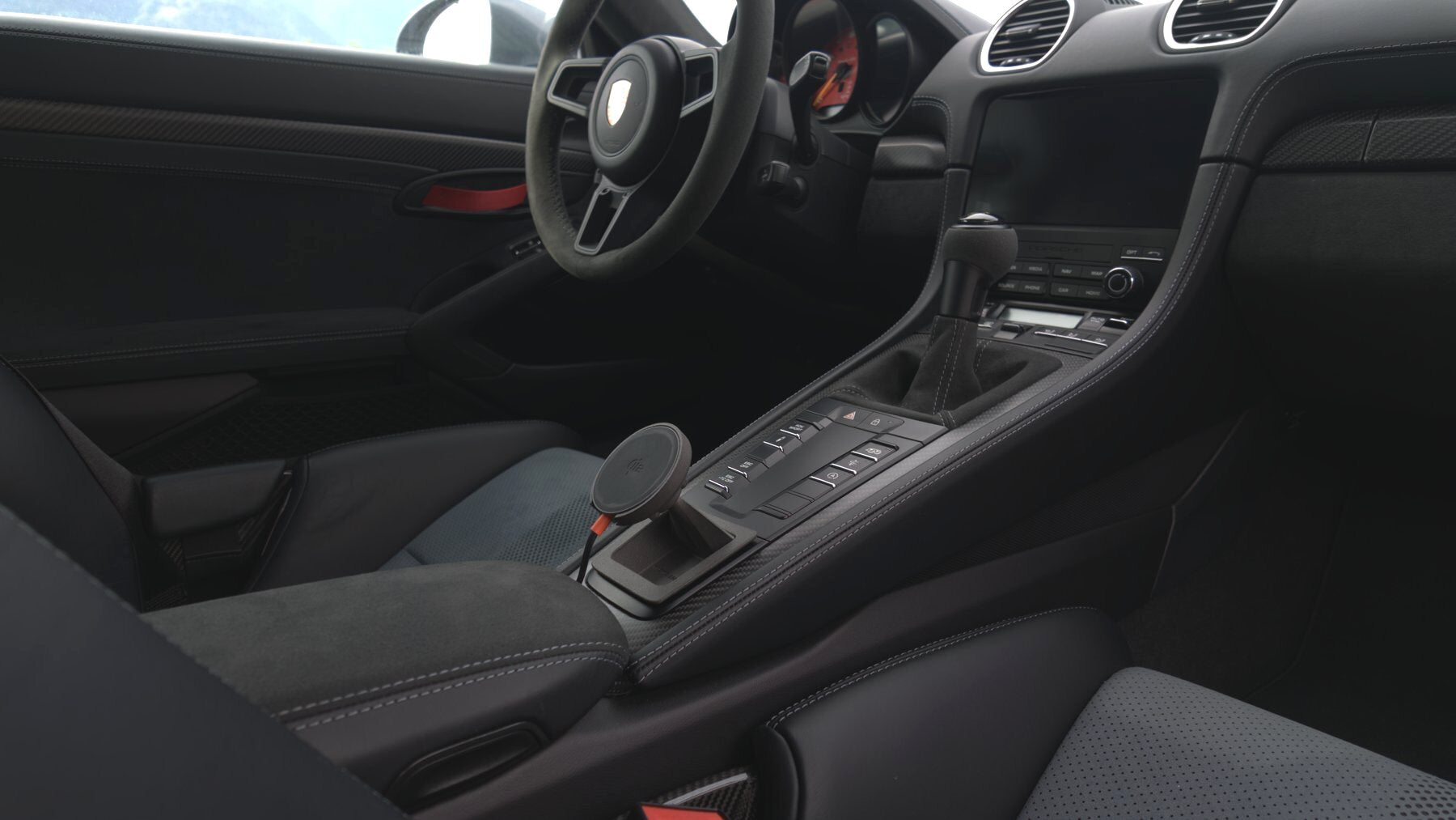 Tactic Engineering magnetic MagSafe phone mount installed in the open centre console tray of a Porsche 718 Cayman GT4 RS interior with Alcantara and contrast stitching, no drilling
