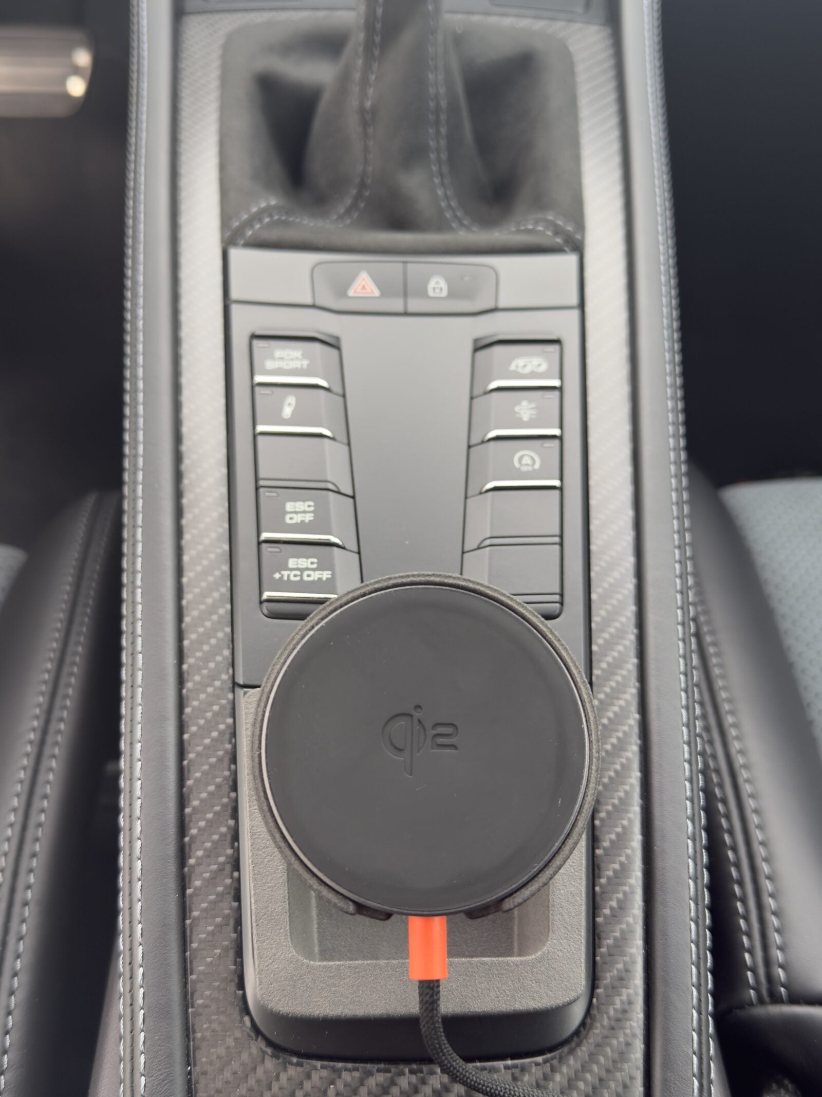 Tactic Engineering MagSafe Qi2 phone mount in the open centre console tray of a Porsche 718 with carbon fiber trim and PDK Sport buttons, no drilling